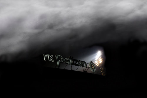 Stadion FK Partizan u noći, sa upaljenim reflektorom koji baca svetlost na slova FK Partizan i grb Partizana.